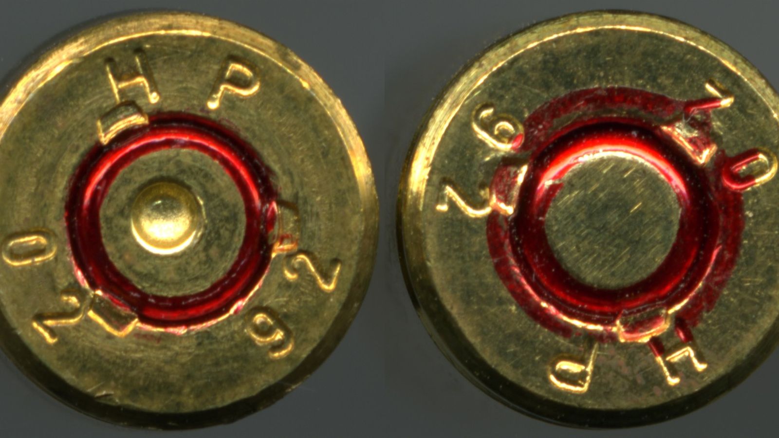 Base de dois cartuchos de fuzil com letras e números gravados no metal, sobre fundo cinza