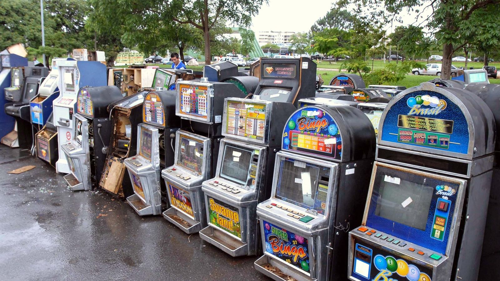 Fileira de máquinas caça-níquel apreendidas, com telas e painéis coloridos, num estacionamento ao ar livre em Brasília